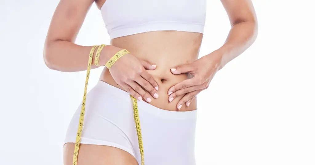 Woman in white underwear measuring her waist with a yellow tape for Liposuction in Suwanee, GA.