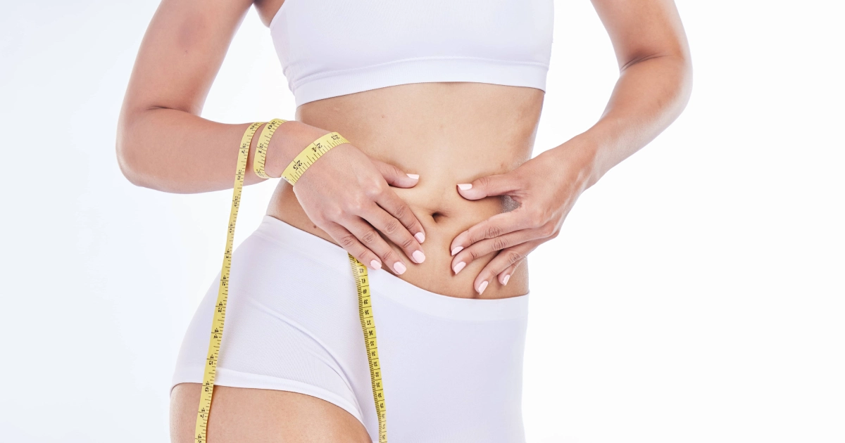 Woman in white underwear measuring her waist with a yellow tape for Liposuction in Suwanee, GA.